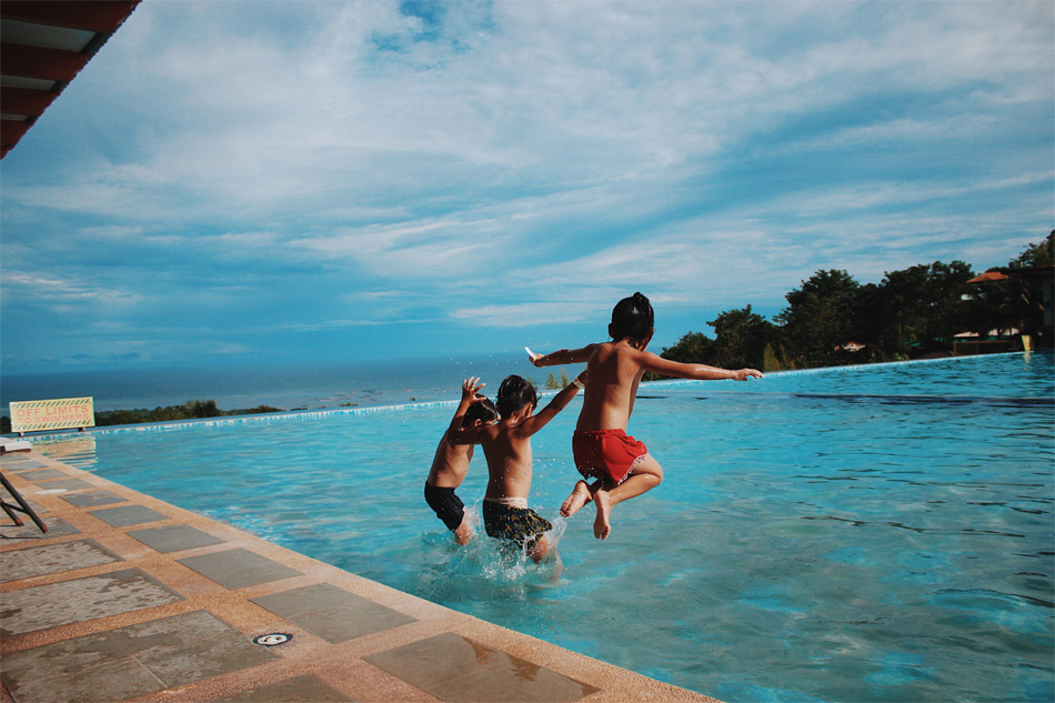 Three kids jumping in a swimming pool
